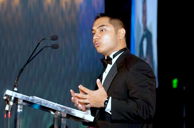 Giovan Bazan at a podium in a tuxedo
