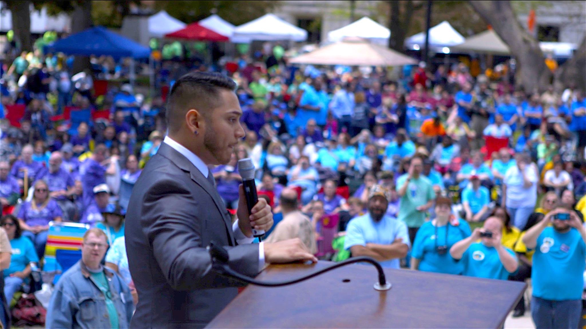 Giovan Bazan speaking to a large outdoor crowd